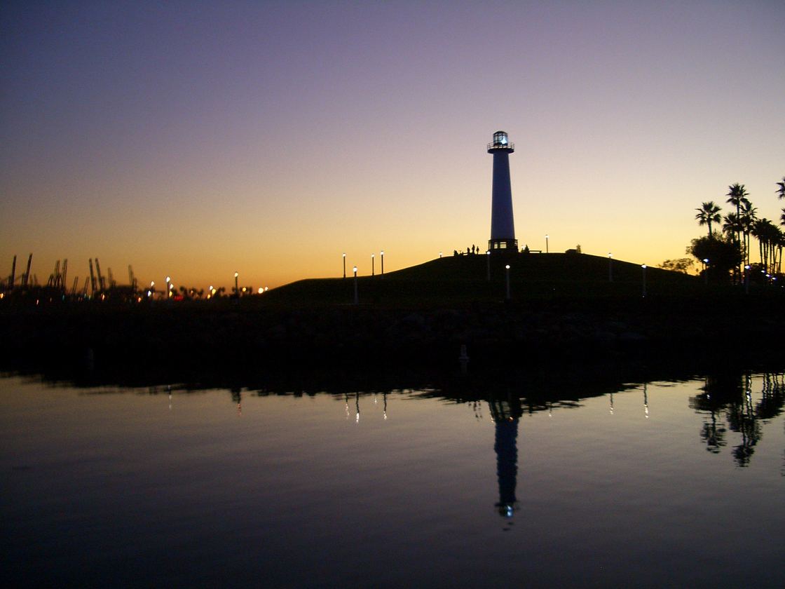 The Lions Lighthouse in Shoreline Aquatic Park silhouetted against an orange sunset, reflected in the still water of the harbor