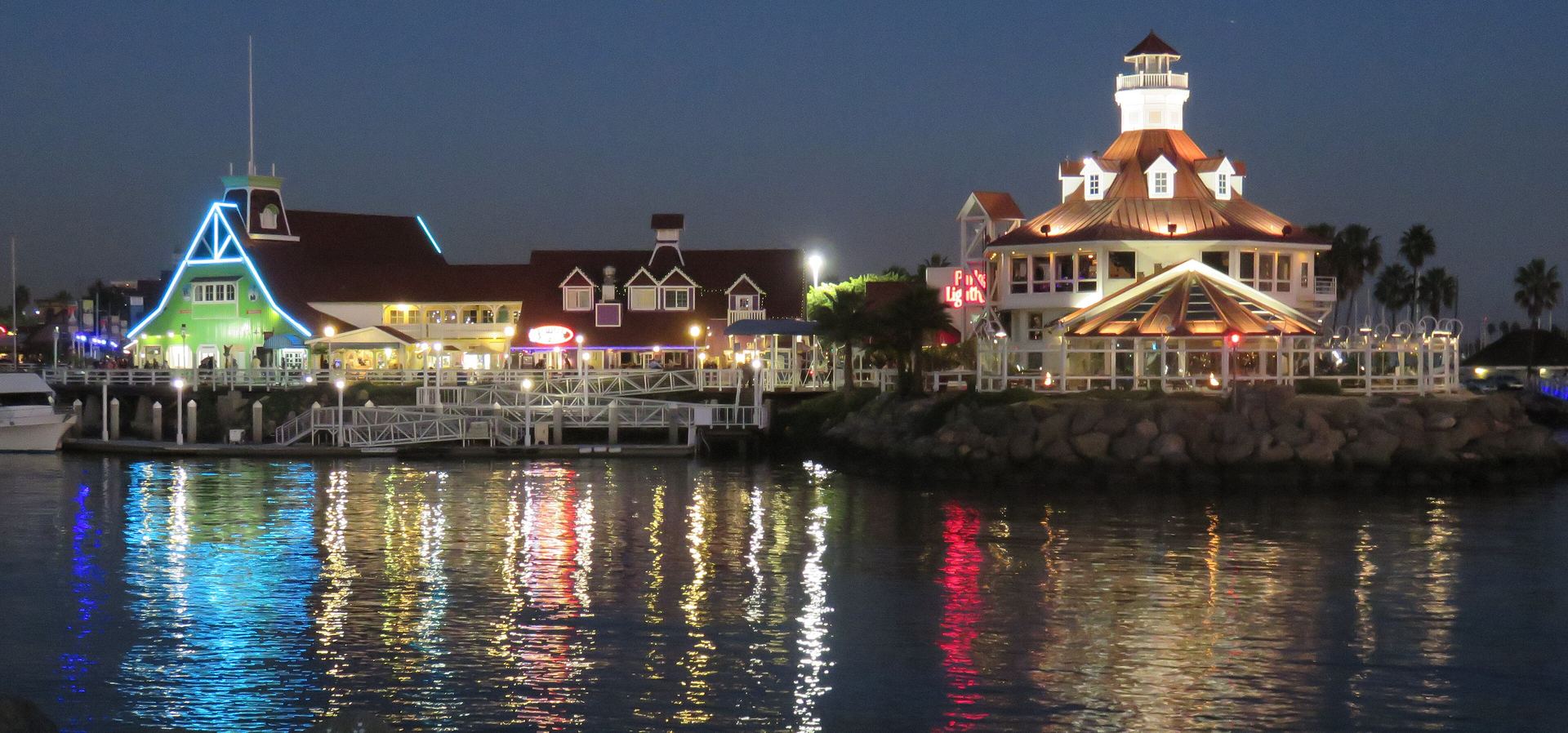 Shoreline Village and Parker’s Lighthouse lit up at night, reflected in Rainbow Harbor